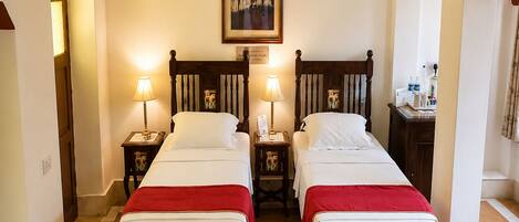 A hotel room with two wooden beds, a painting on the wall, and a small table with a lamp.