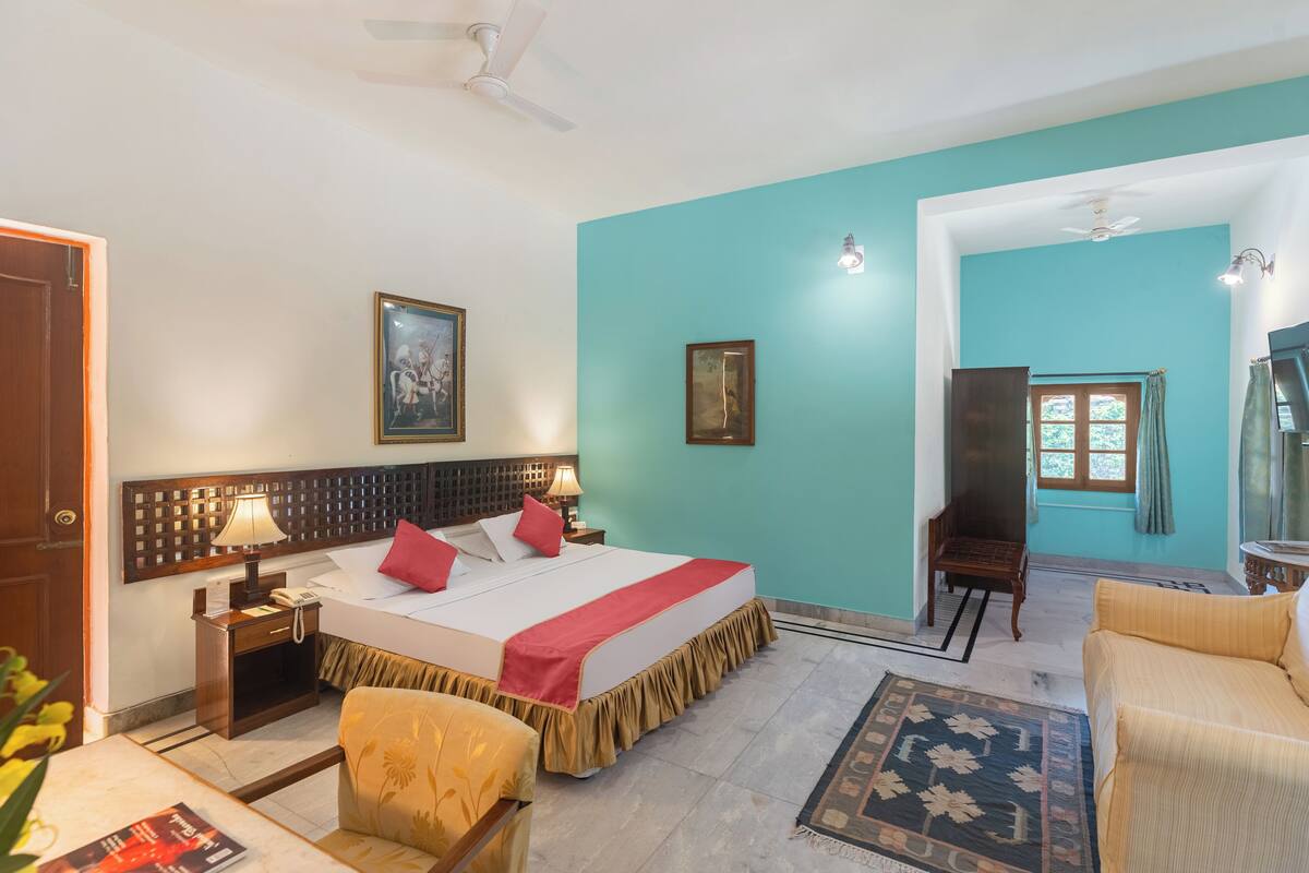 A hotel room with a bed, bedside table, lamp, chair, and a view of the outside.