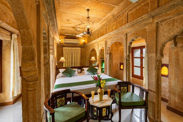 Une chambre d’hôtel avec un grand lit, deux fauteuils, une table avec des boissons et un vase décoratif.