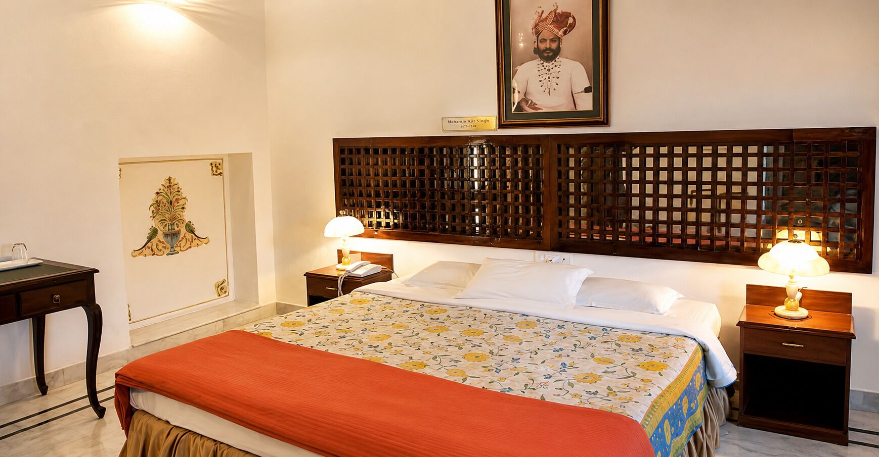 Una habitación de hotel con una cama, dos mesitas de noche, una lámpara, un cuadro enmarcado en la pared y un biombo sobre la cama.