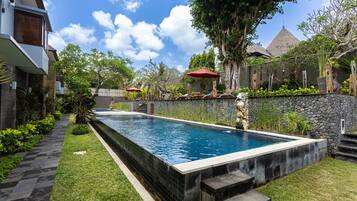 A rectangular swimming pool with a stone border, surrounded by a stone wall and a grassy area with steps leading to the pool.