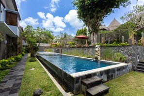 A rectangular swimming pool with a stone border, surrounded by a stone wall and a grassy area with steps leading to the pool. - Abi Bali Resort Villas & Spa (Jimbaran)
