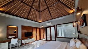 A modern hotel room with a large bed, a desk, a TV, and a bathroom with a glass shower. - Abi Bali Resort Villas & Spa (Jimbaran)