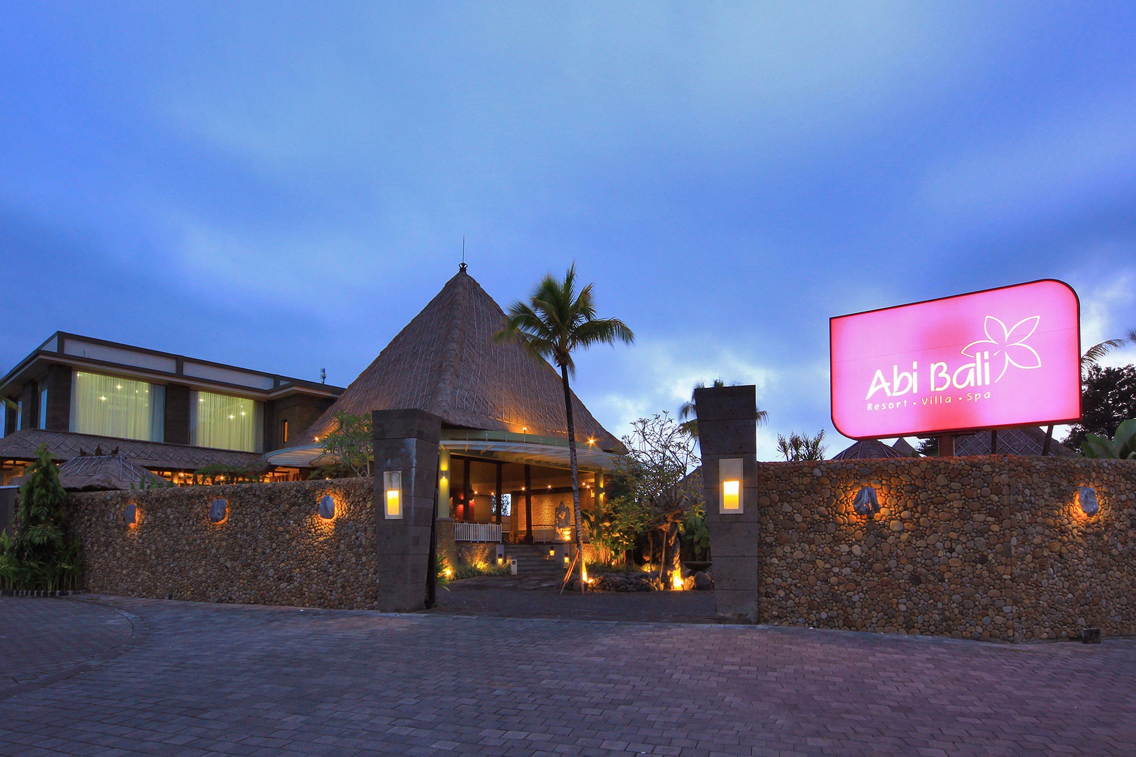 A resort with a thatched-roof building, stone walls, and a large illuminated sign.