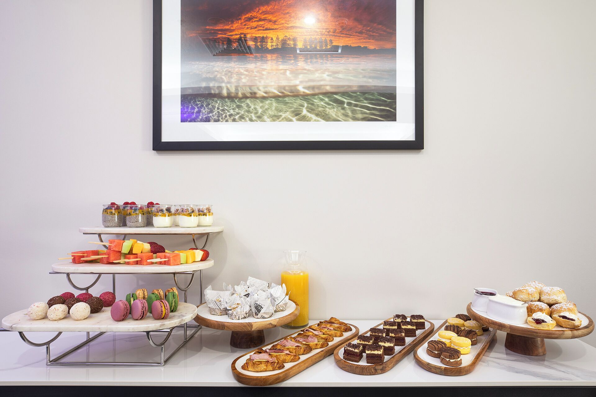 A breakfast buffet with various food items and a framed picture of a sunset over water.