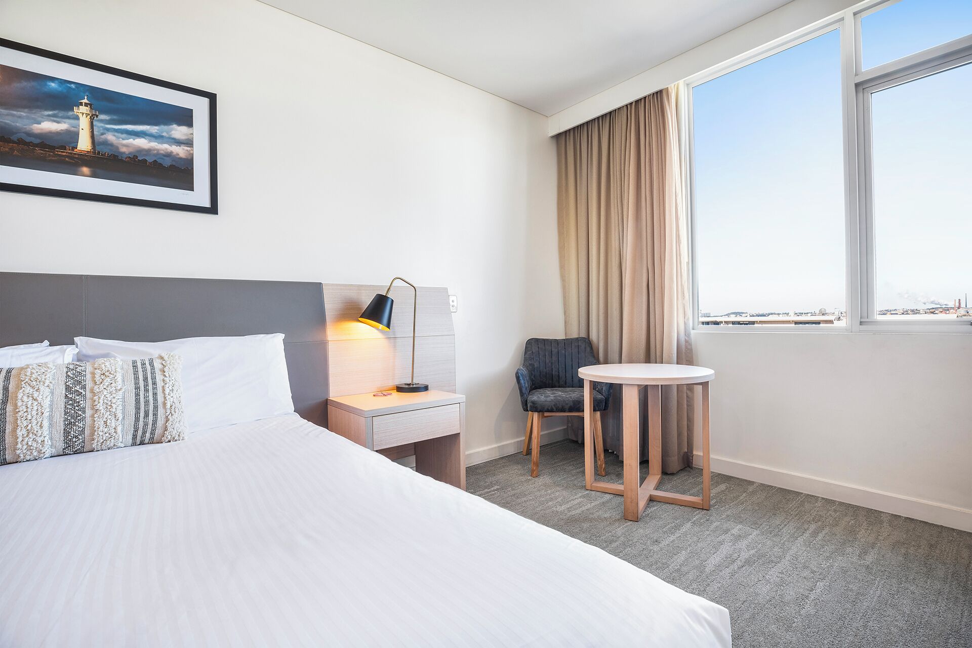 Une chambre d’hôtel avec un lit, une table de chevet, une lampe, une chaise et une fenêtre donnant sur un paysage agréable.