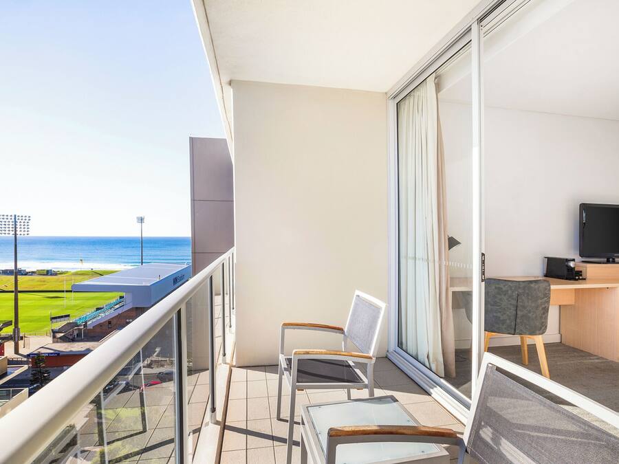 A balcony with a view of the ocean, a desk with a TV, and two chairs.
