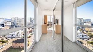Un estrecho pasillo con ventanas amplias que conduce a una habitación con escritorio y silla, y vistas de la ciudad.