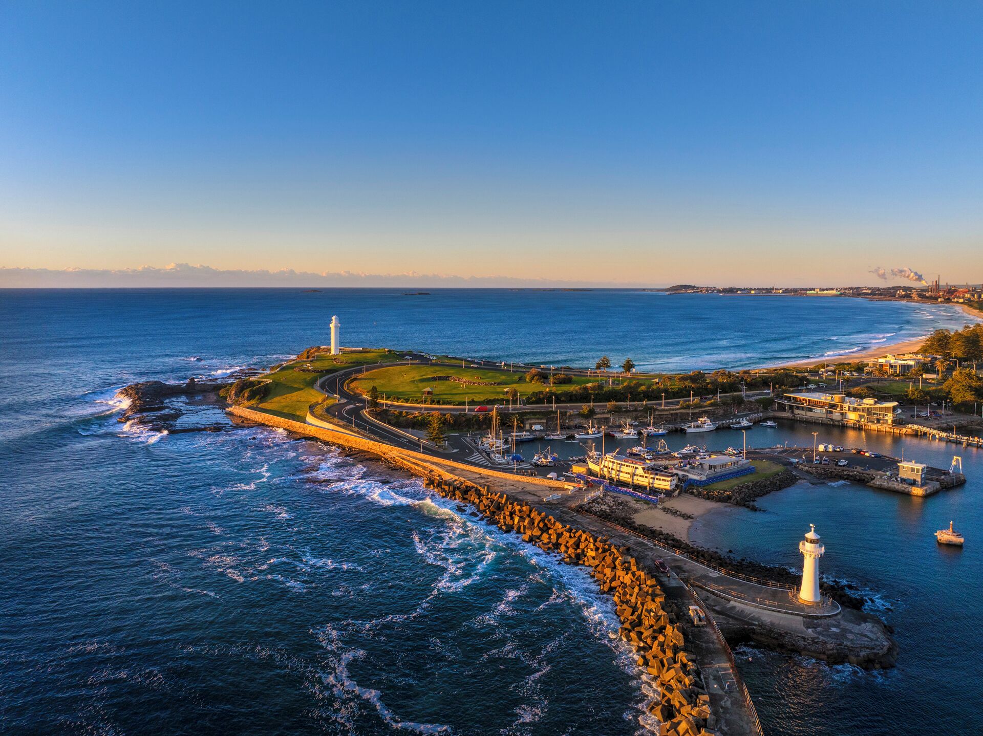 A coastal area with a lighthouse, a marina with boats, and a curved road leading to the shore.
