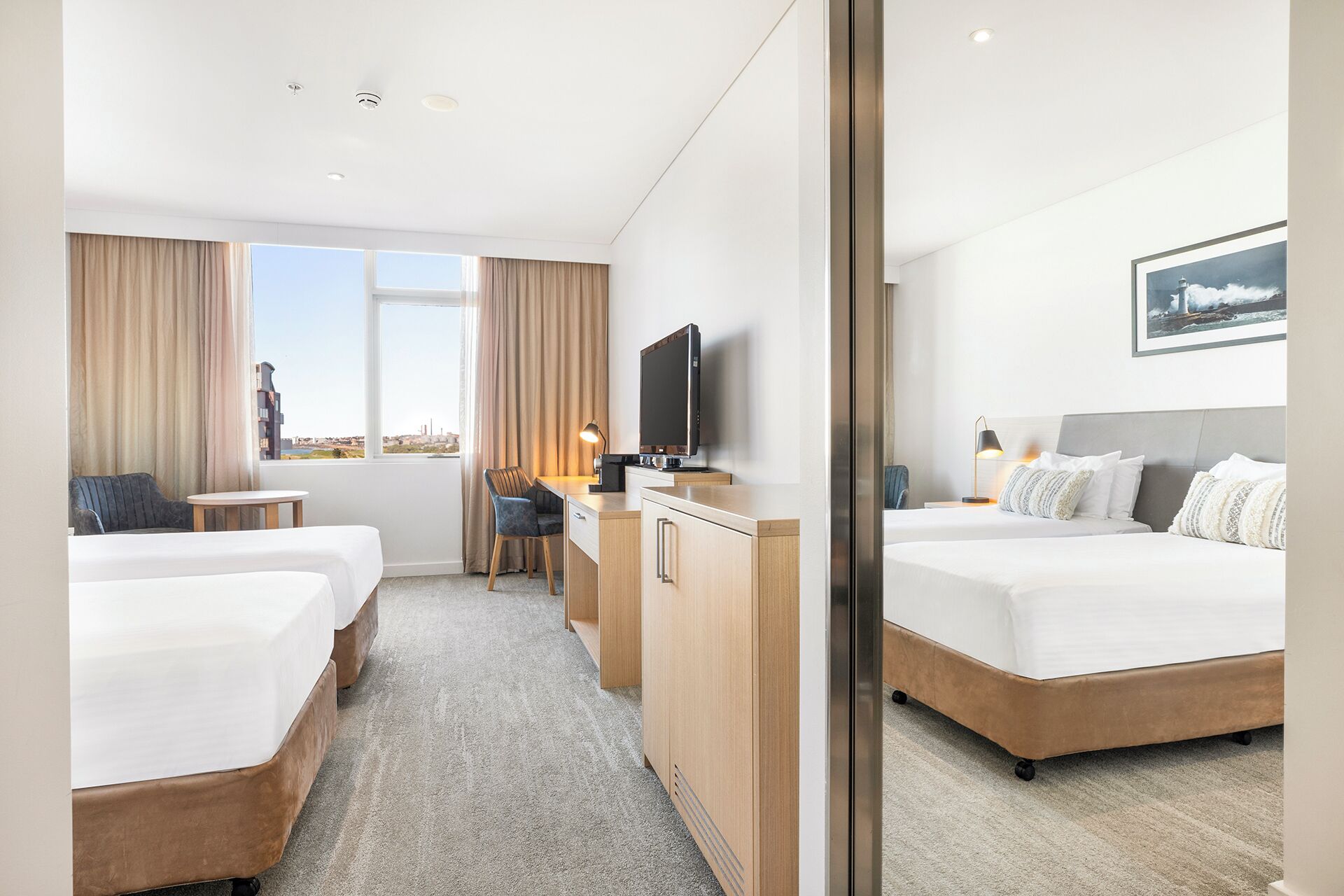 Habitación de hotel con dos camas, un escritorio, una silla, un televisor y vistas a la ciudad.