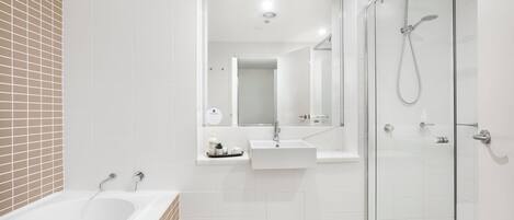 Un baño moderno con bañera, ducha con mampara de vidrio y tocador con espejo.