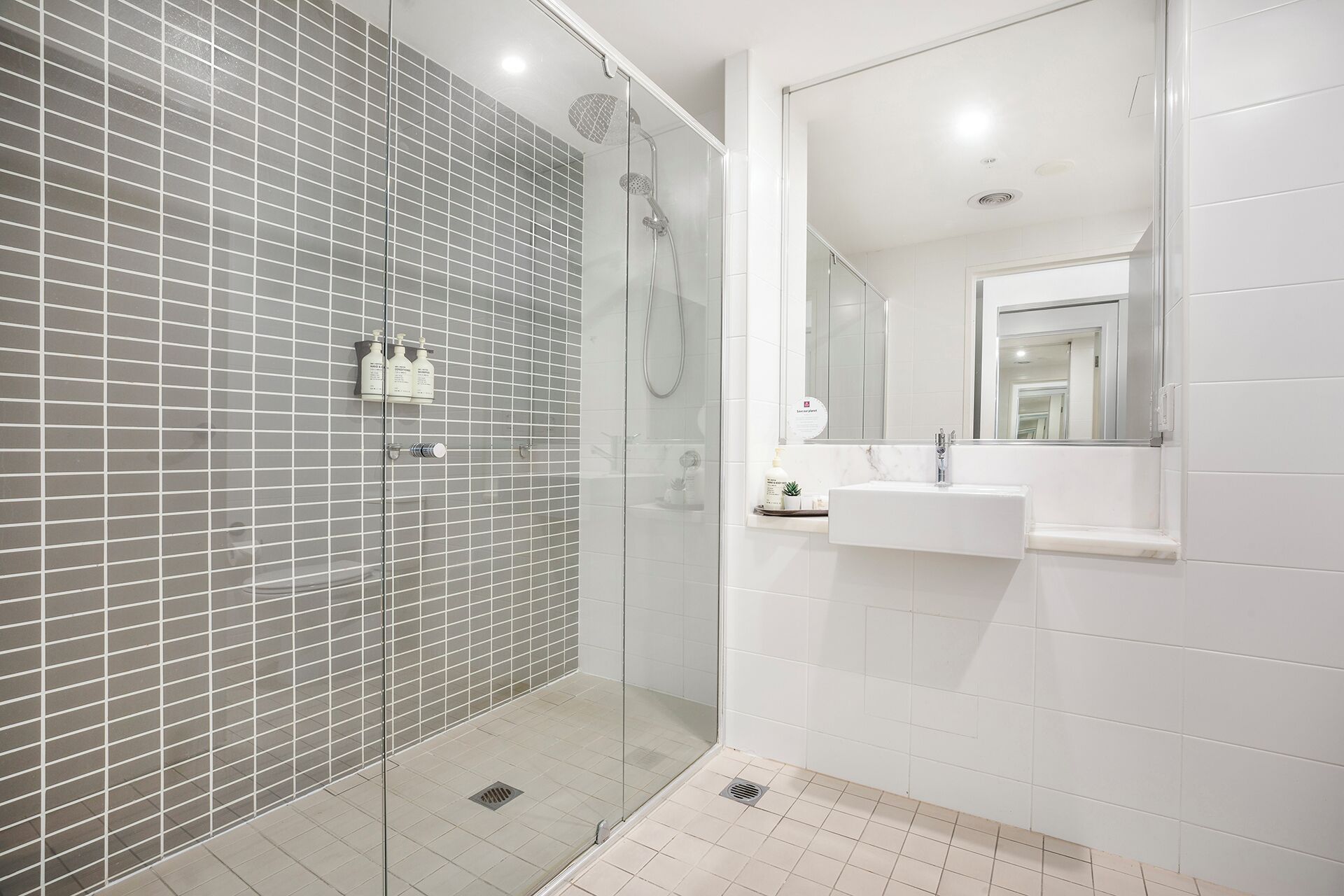 A modern bathroom with a glass-enclosed shower, a white sink, and a large mirror.