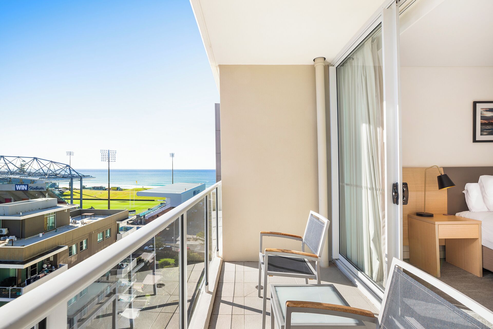 Ein Balkon mit Blick auf ein Stadion und den Ozean. Zwei Stühle und ein kleiner Tisch sind vorhanden.