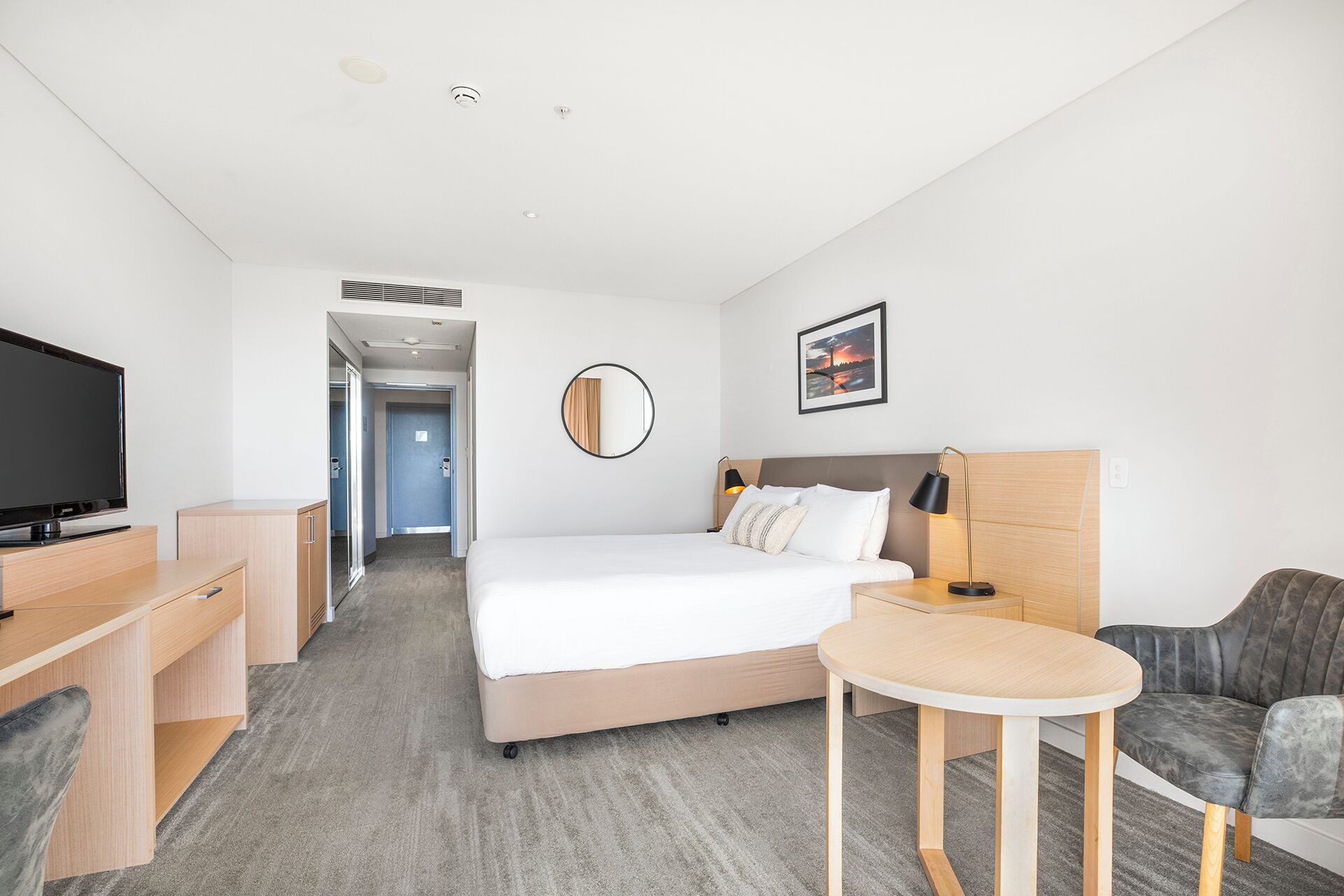 Una habitación de hotel con cama, escritorio, silla, televisor y una pequeña mesa.