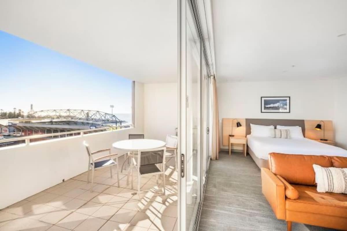 Habitación de hotel con balcón, una cama, un sofá, una mesita y una silla.