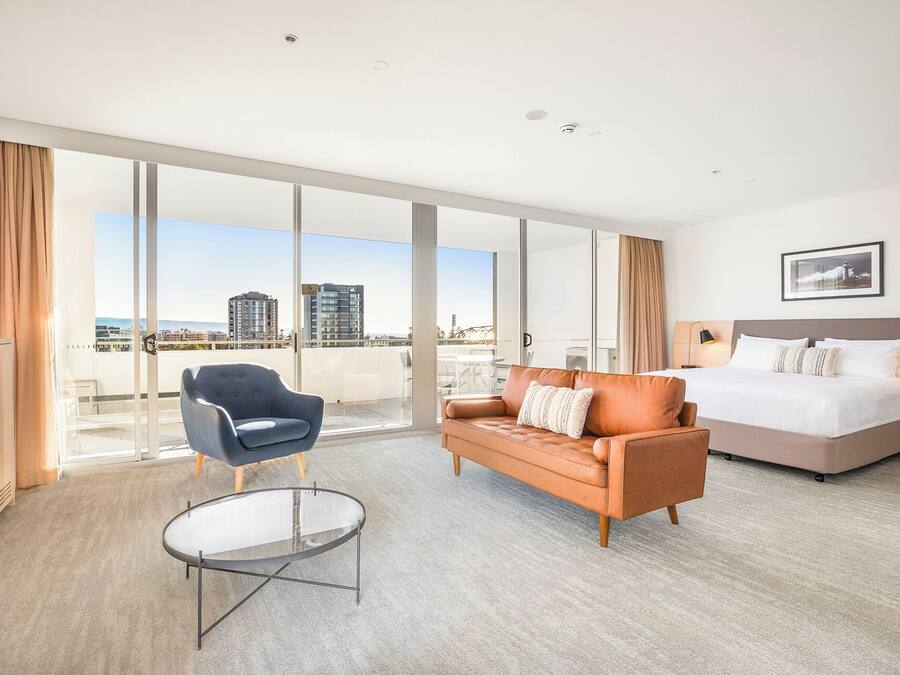 A hotel room with a large bed, a sofa, a chair, and a glass coffee table.