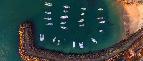 An aerial view of a marina with boats docked and a rocky breakwater surrounding a sandy beach.