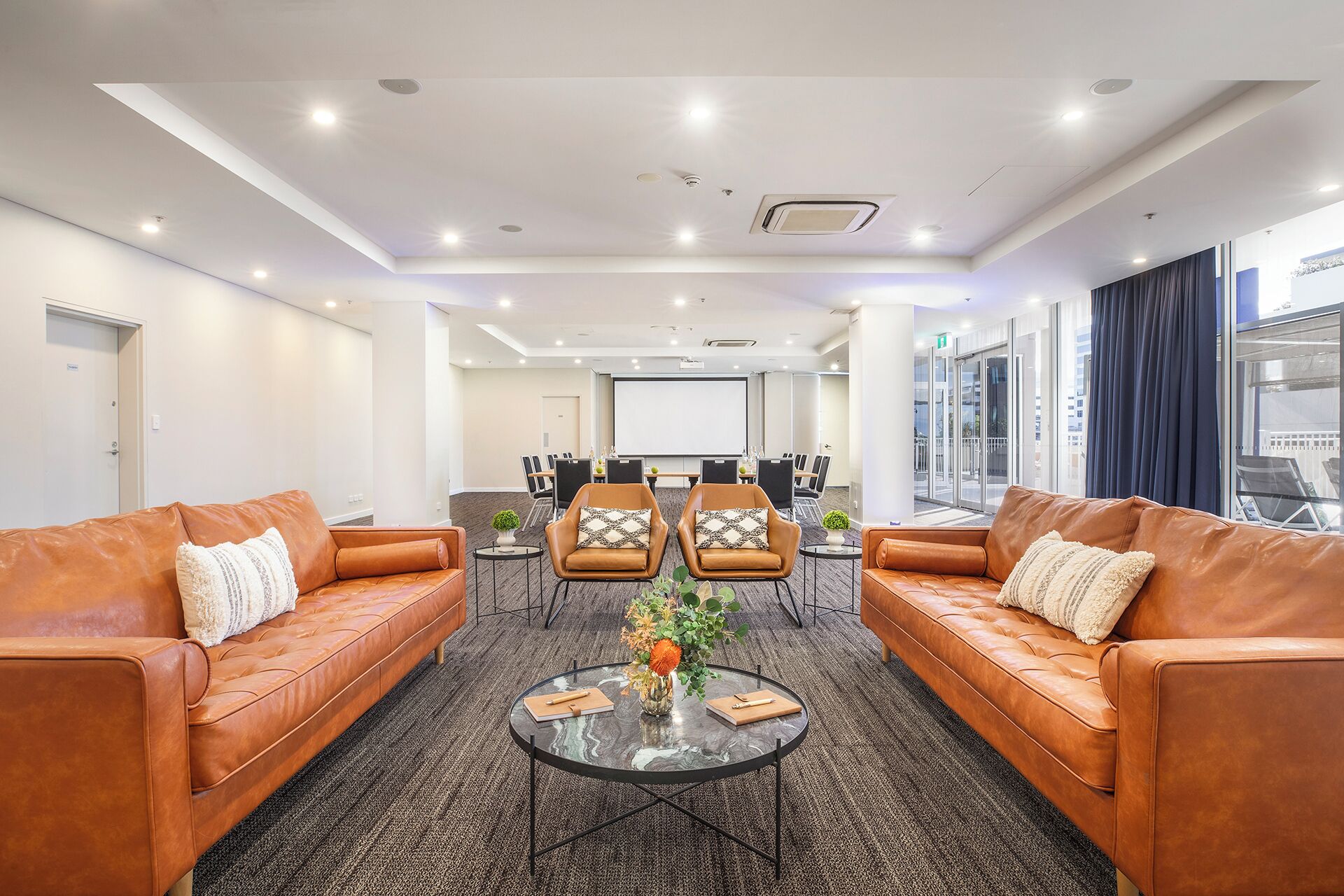 A modern hotel lobby with leather sofas, a conference table, and a large screen.