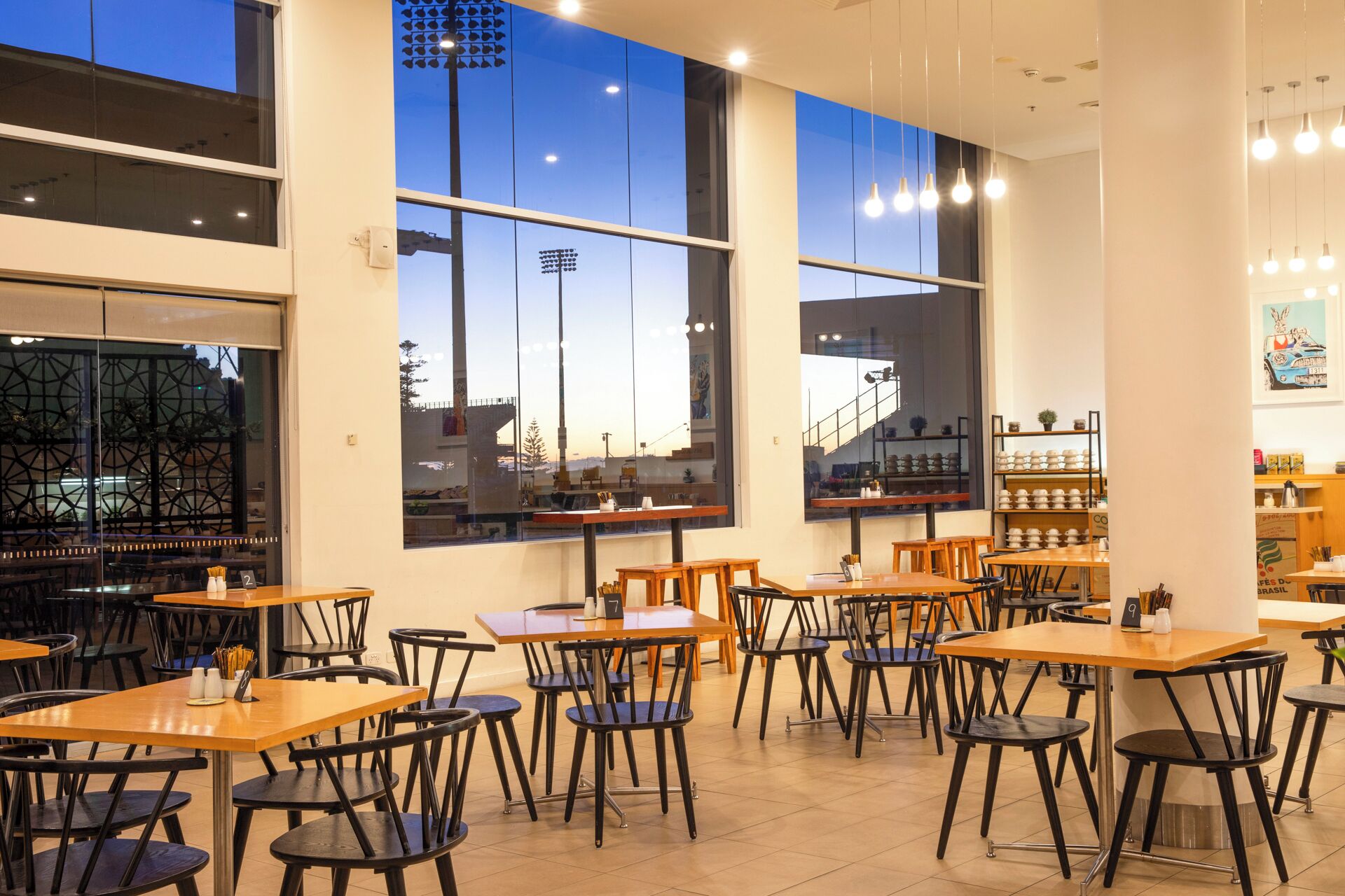 A modern restaurant with multiple tables and chairs, large windows with city views, and a clean, contemporary interior design.
