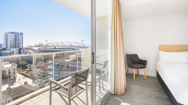 A hotel room with a balcony, a bed, and a chair. - Sage Hotel Wollongong (Wollongong)