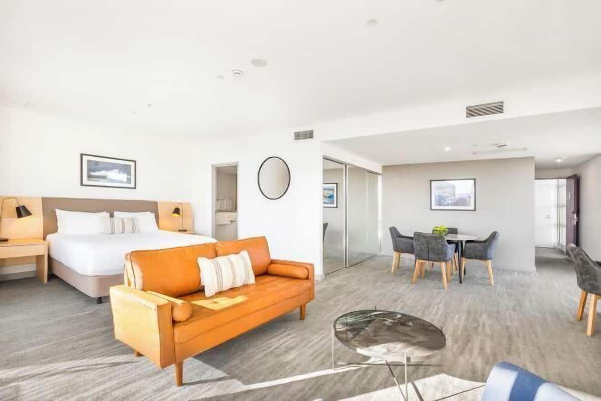 A hotel room with a bed, a sofa, a dining table with chairs, and a small coffee table.