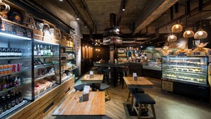 L’intérieur d’un restaurant avec des tables en bois, un coin bar et une vitrine où sont exposées des pâtisseries.