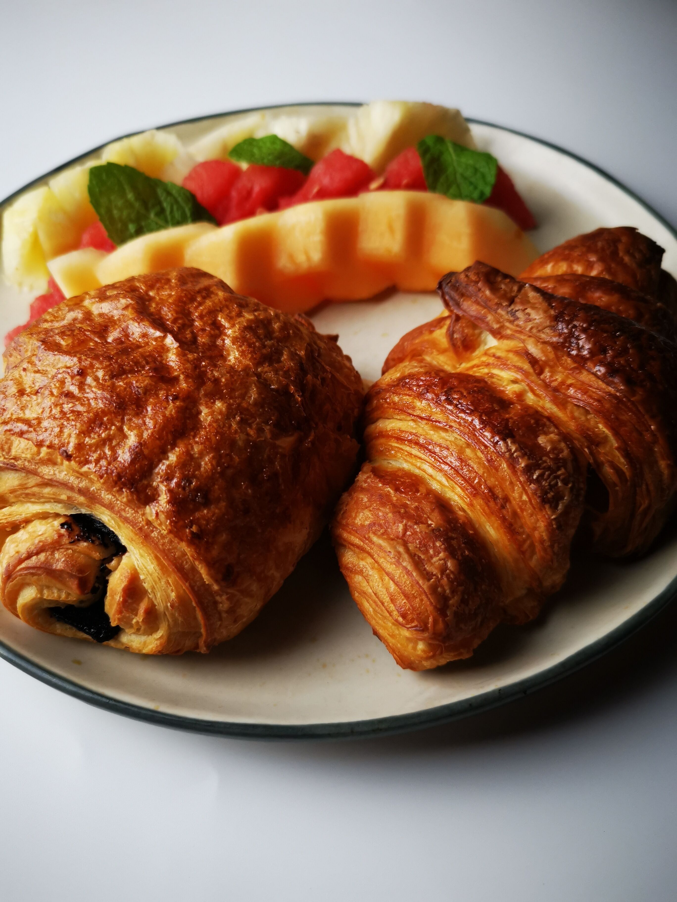 A plate with two croissants and a fruit salad.