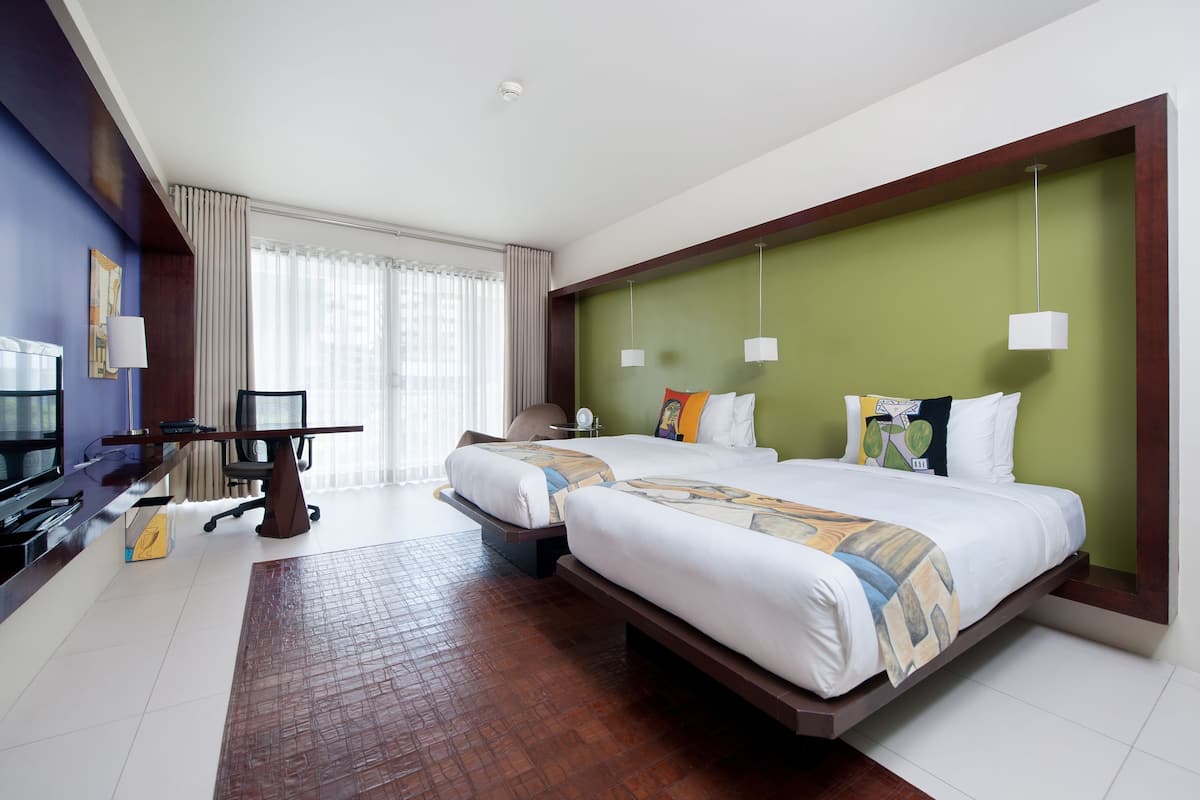 Une chambre d’hôtel avec deux lits, un bureau, une télévision et une grande fenêtre avec des rideaux.
