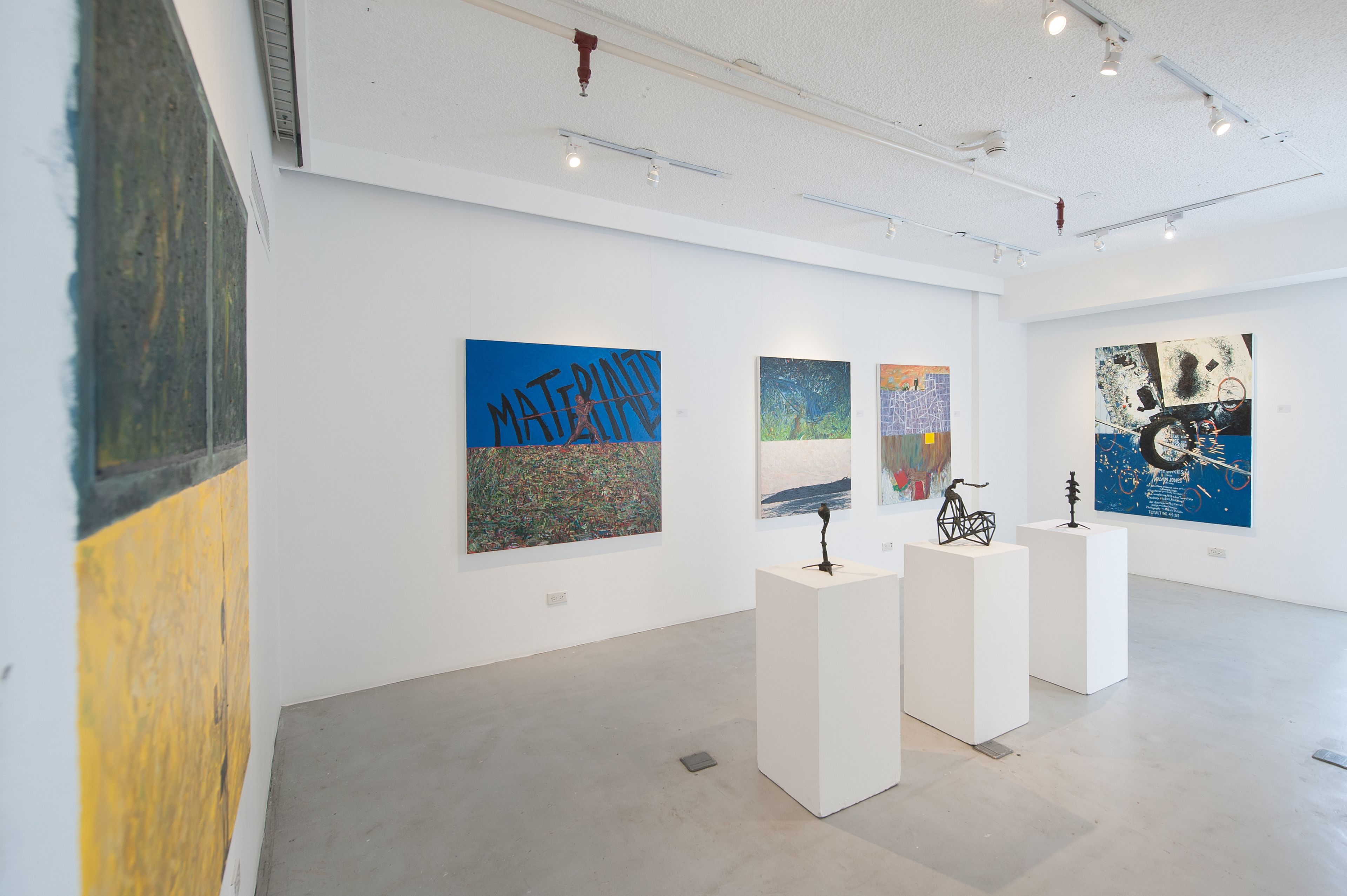 An art gallery with white walls and a concrete floor, featuring various abstract paintings displayed on white pedestals.
