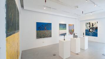 An art gallery with white walls and a concrete floor, featuring various abstract paintings displayed on white pedestals.