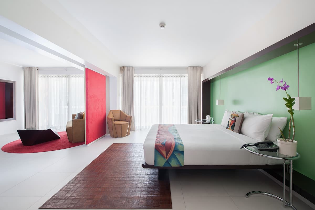 Une chambre d’hôtel moderne avec un grand lit, un mur d’accent rouge, un mur d’accent vert, une orchidée en pot et un bureau avec un téléphone.