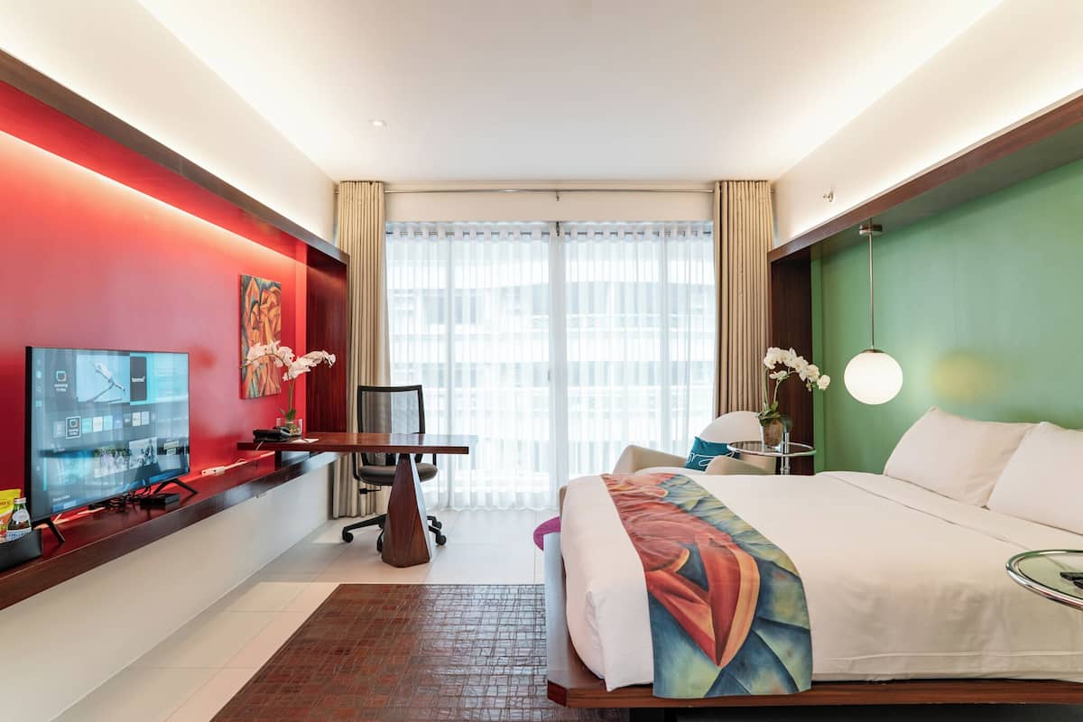 Une chambre d’hôtel avec un lit, un bureau avec un ordinateur, une télévision et une fenêtre avec des rideaux.