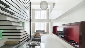 Un salon moderne avec un canapé, un coin repas doté d’une table en verre et un téléviseur placé contre un mur rouge.