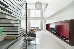 A modern living room with a sofa, a dining area with a glass table, and a TV against a red wall. - The Picasso Boutique Serviced Residences (Makati)