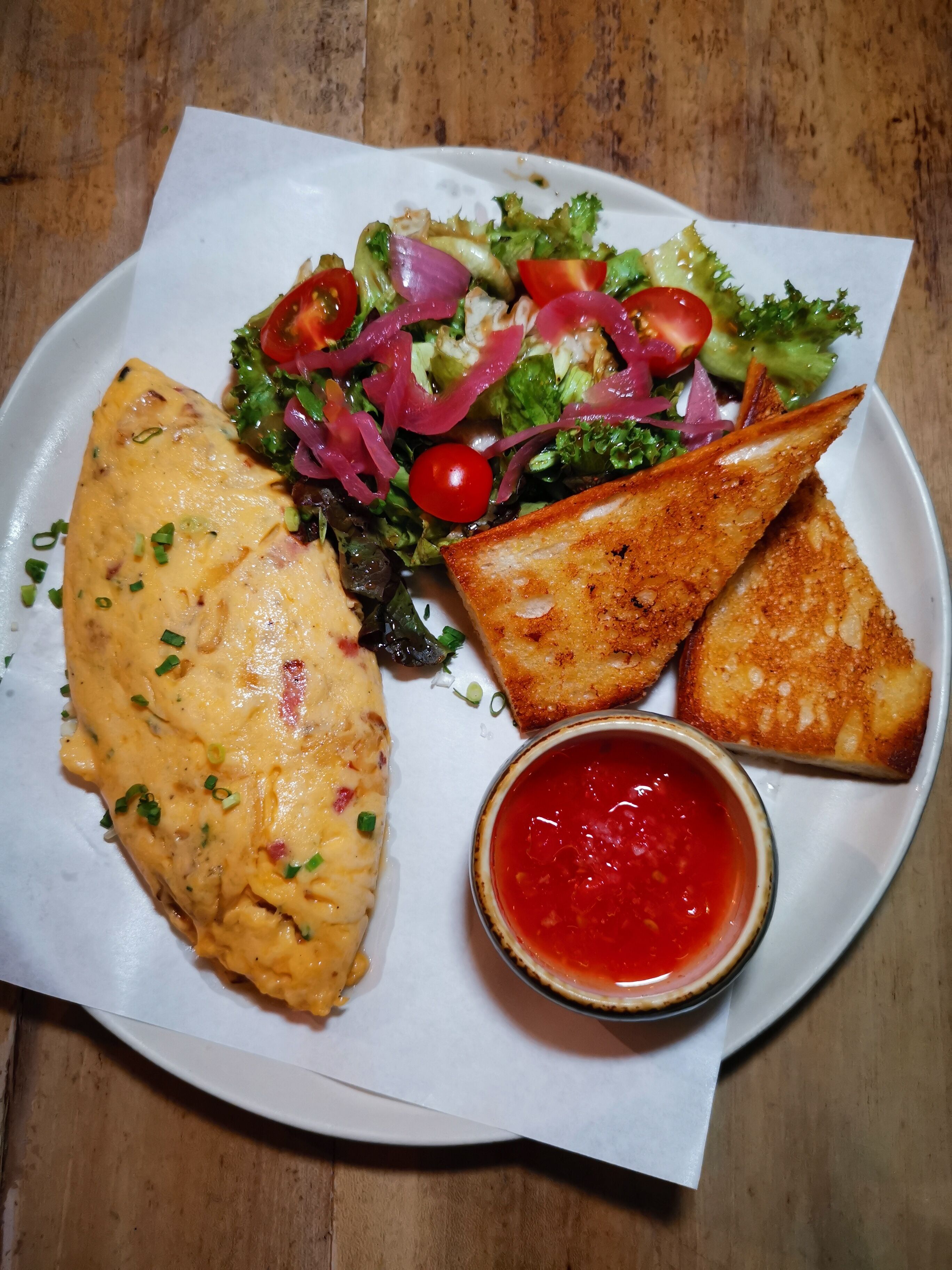 Ein Teller mit einem gegrillten Omelett, Salat, geröstetem Brot und einer kleinen Soße.