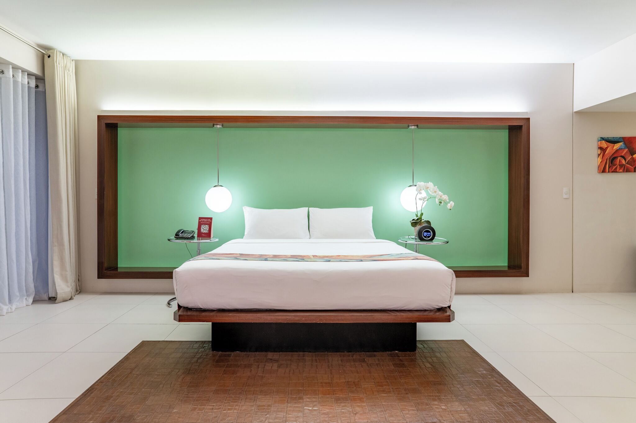 Een moderne hotelkamer met een groot bed, een groene accentmuur, nachtkastjes met lampen en een schilderij aan de muur.