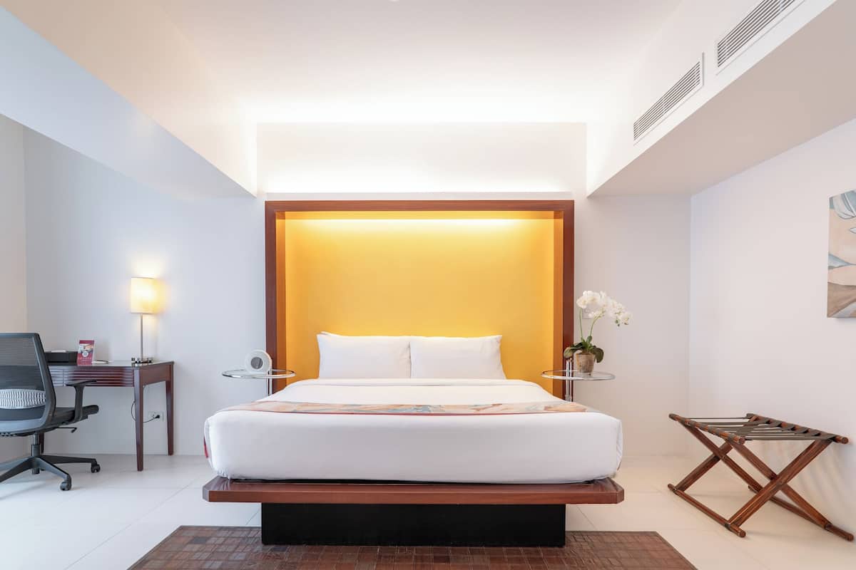 Une chambre d’hôtel moderne avec un grand lit, des tables de chevet, un bureau avec une chaise, une petite table avec une lampe et un climatiseur fixé au mur.