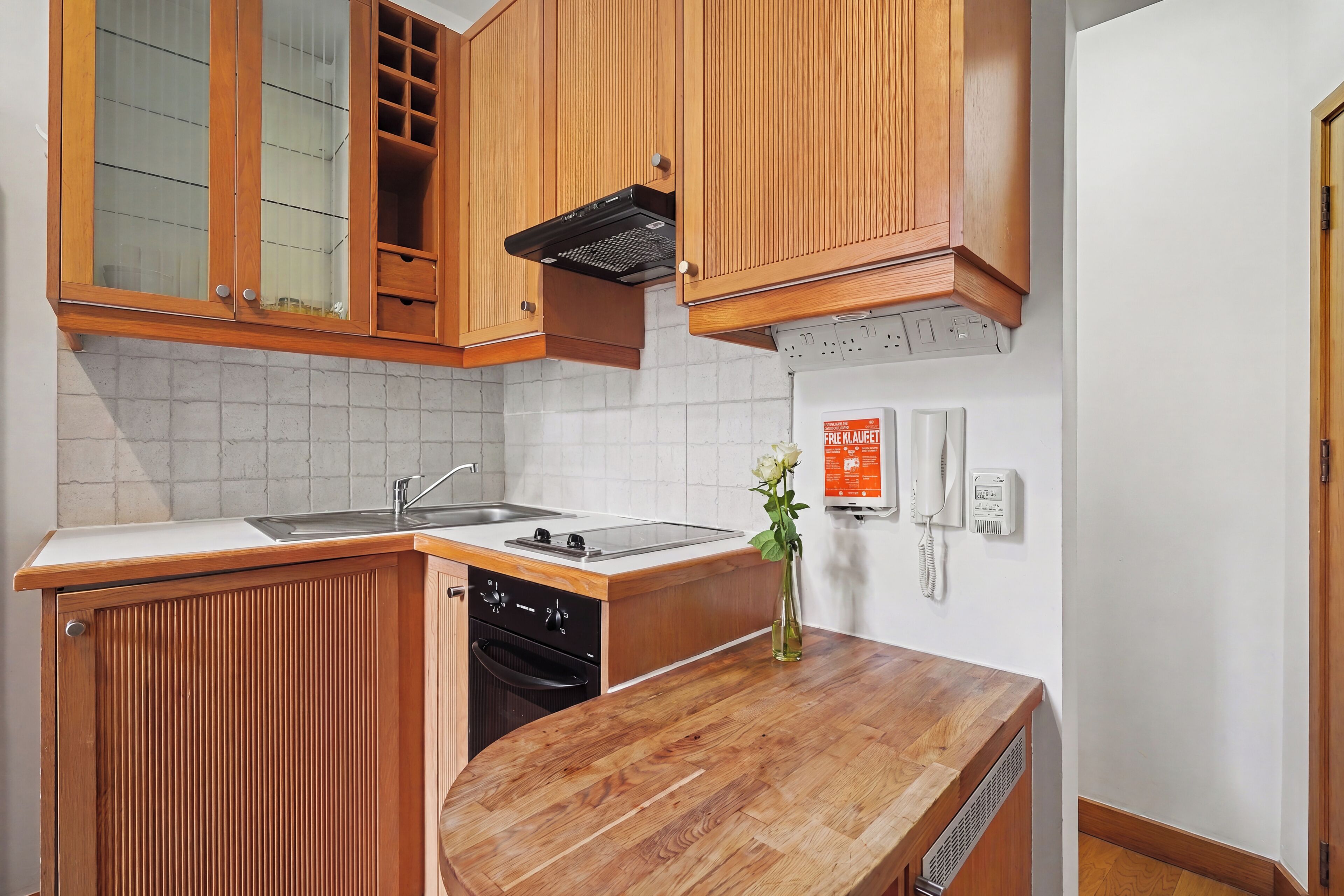 Una cocina compacta con armarios de madera, horno integrado y un lavamanos.