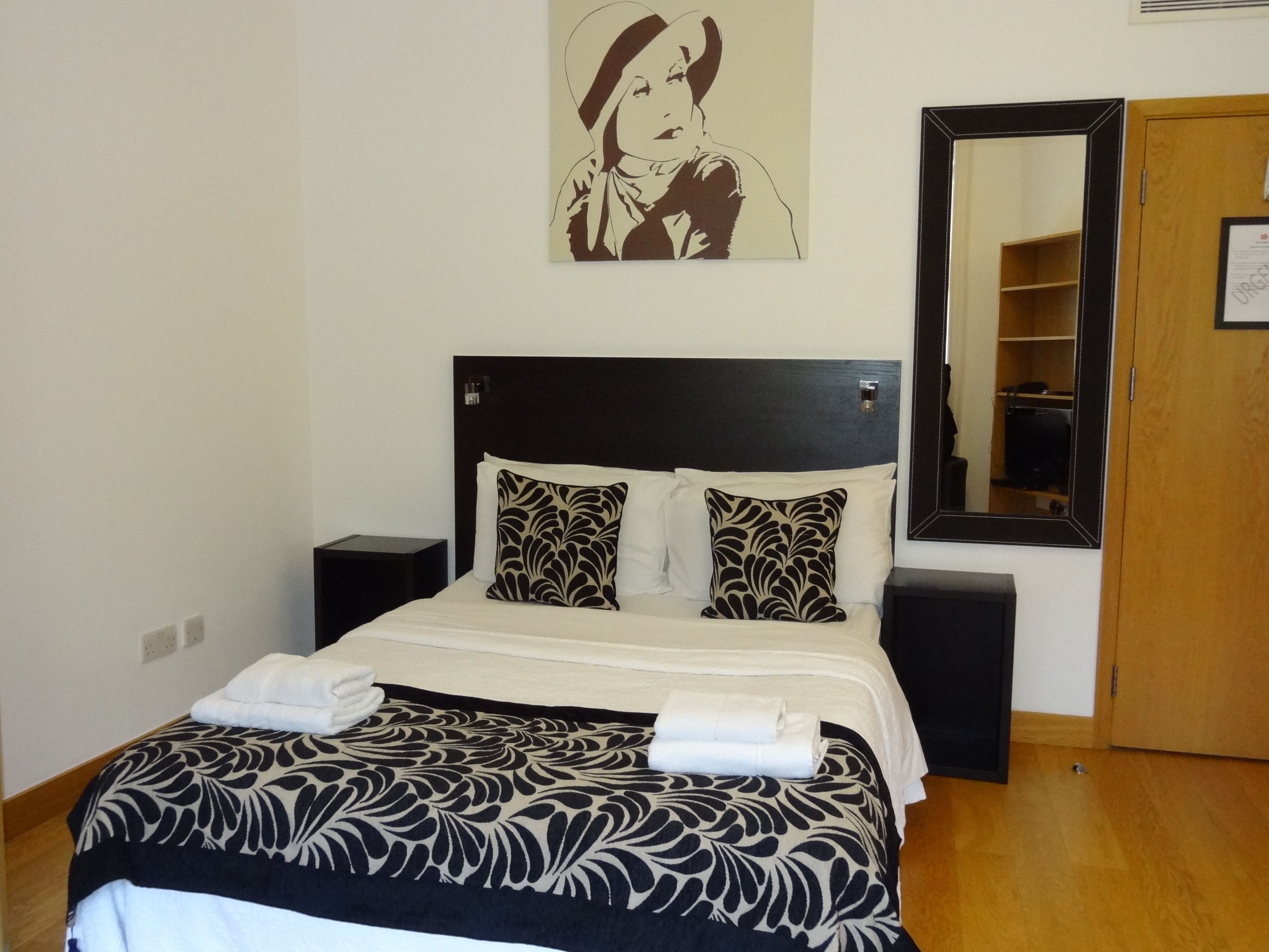 A neatly made bed with patterned bedding, a bedside table, a nightstand, a mirror, and a wardrobe.