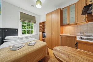 Quarto moderno com cama, janela com vista, guarda-roupa de madeira e kitchenette.