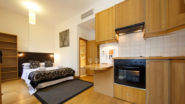 A compact hotel room with a kitchenette, a bed with patterned bedding, and a small dining area.