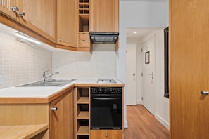 A compact kitchen with a built-in dishwasher, a sink, and wooden cabinets. - Studios2Let Bloomsbury (London)