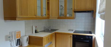 Cocina compacta con gabinetes de madera, lavavajillas, estufa y pileta.