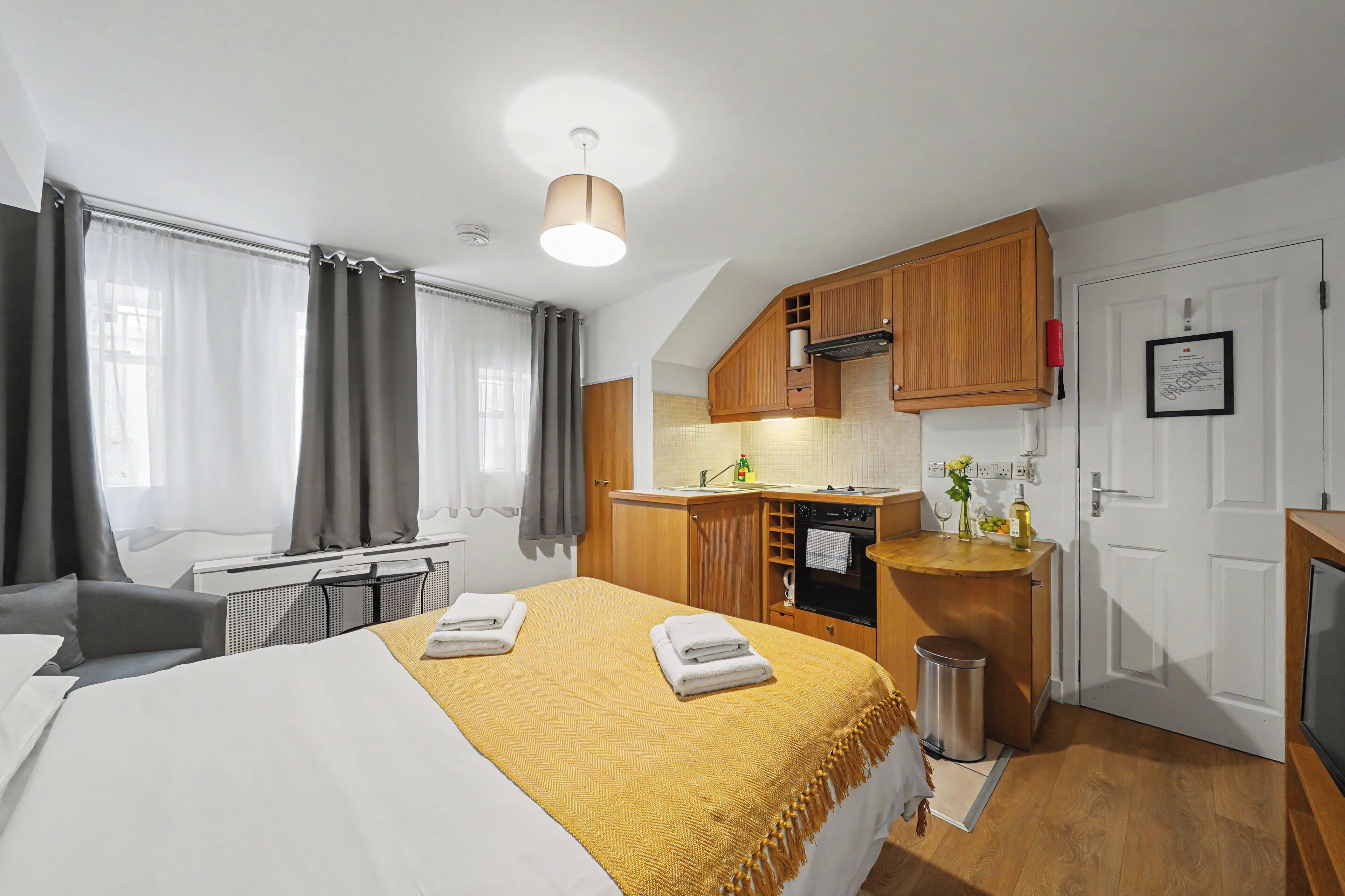 A compact hotel room with a bed, a small kitchenette, and a bathroom.