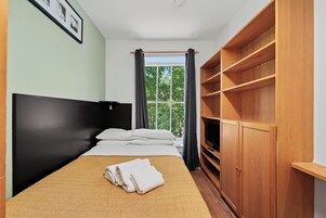 Una habitación de hotel con cama, ventana con cortinas, armario y un cuadro en la pared.