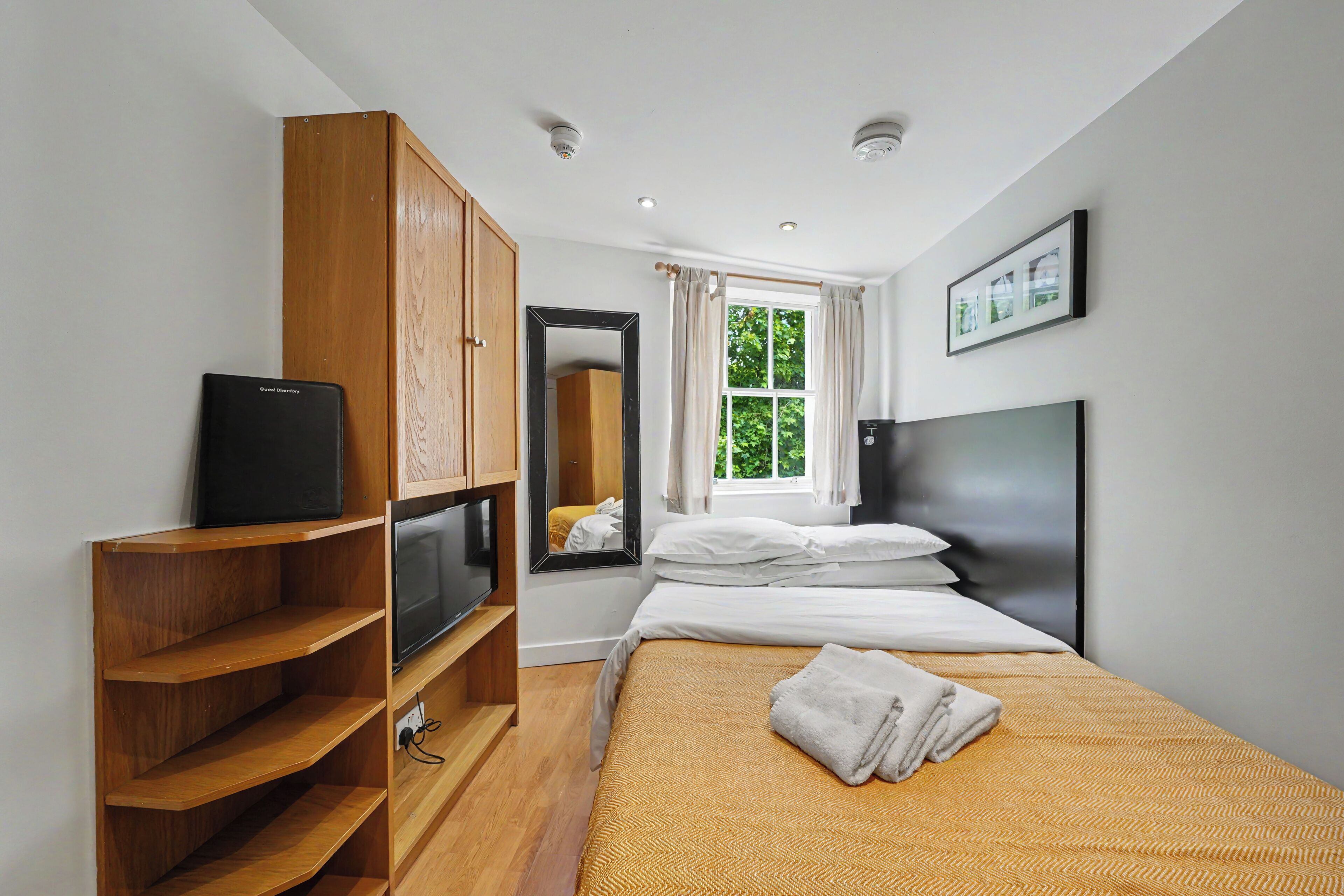 A hotel room with a bed, a TV, a wardrobe, a mirror, and a window with curtains.