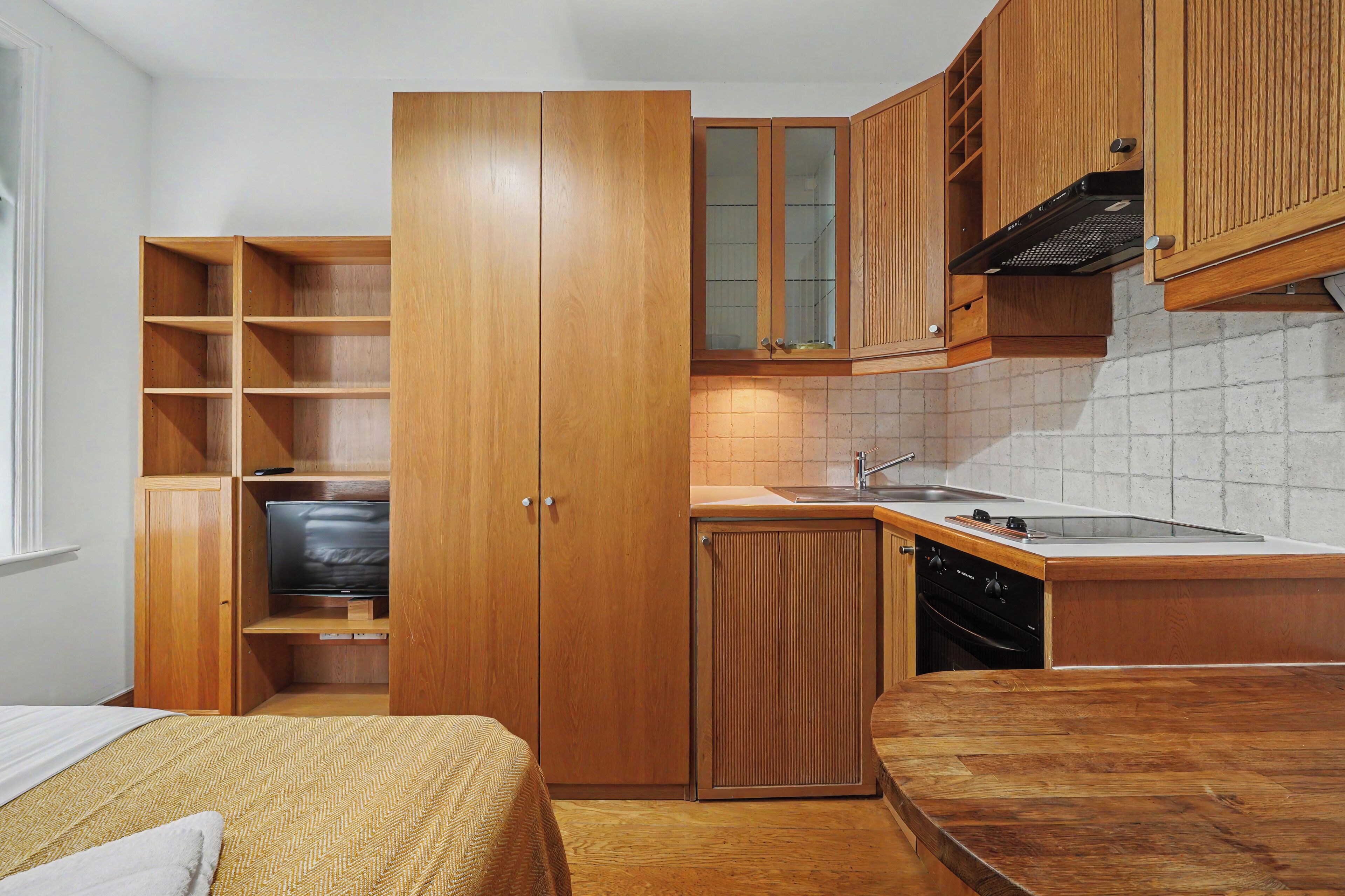 A compact kitchen with wooden cabinets, a built-in TV, and a small countertop with a sink.