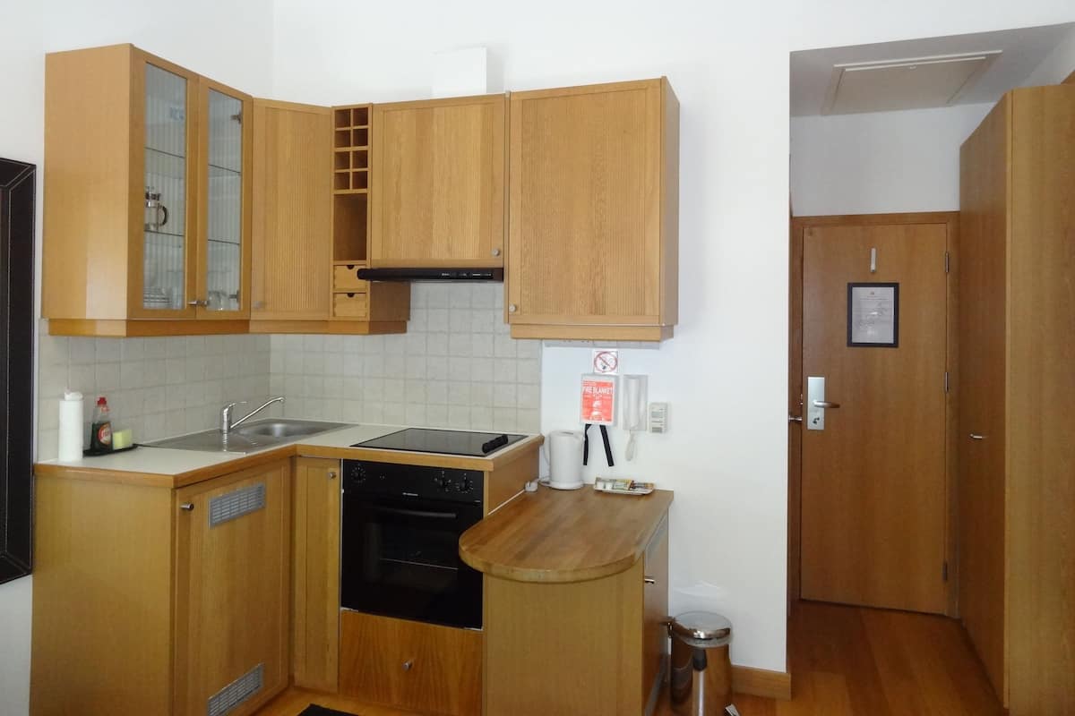 A compact kitchen with wooden cabinets, a built-in oven, a sink, and a stainless steel trash can.