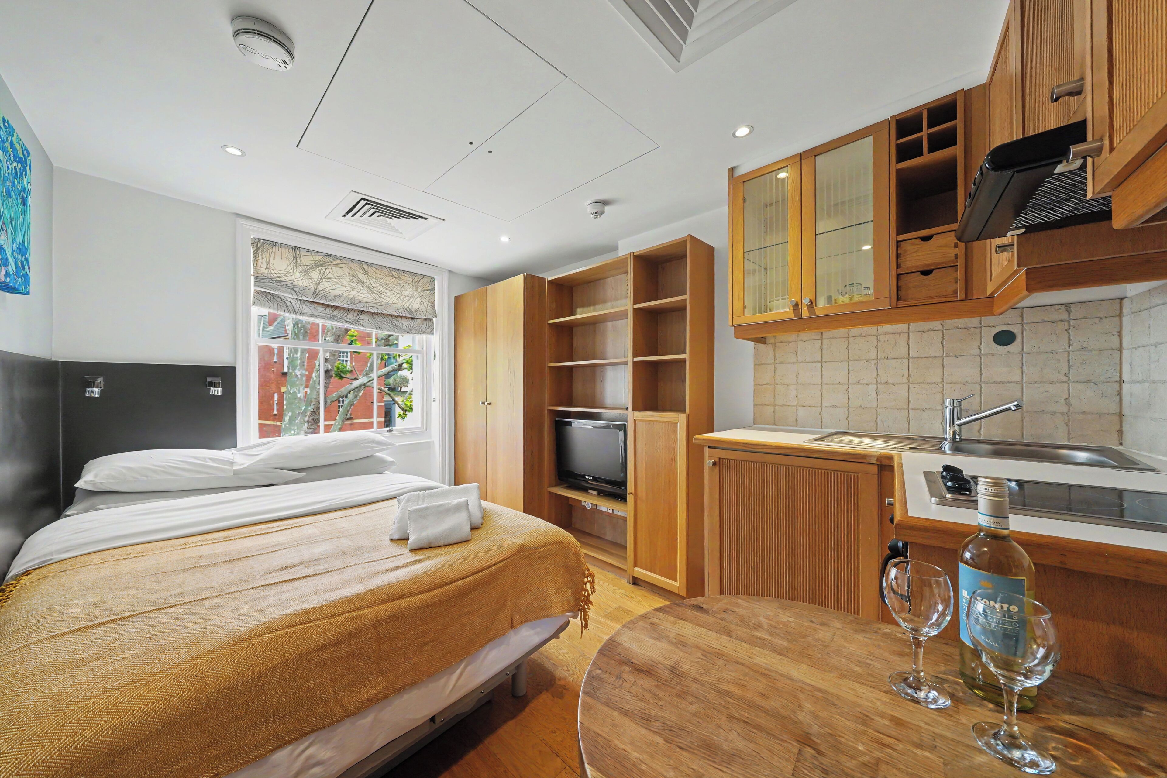 Habitación de hotel con cama, televisor, armarios de madera, kitchenette y ventana con vistas.