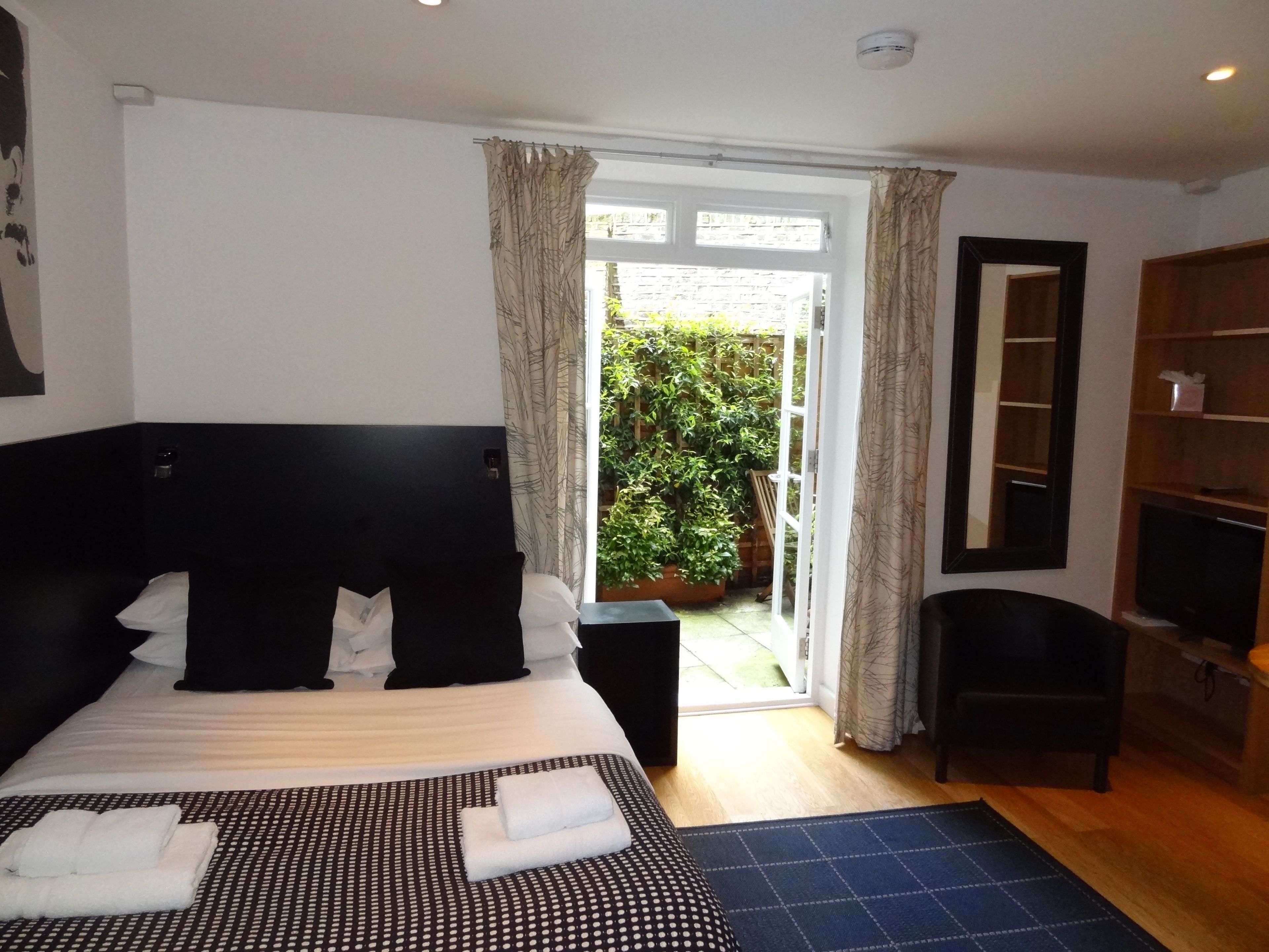 Habitación de hotel con una cama grande, televisión, armario y vista a un jardín a través de una puerta corrediza.